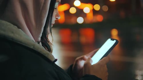 Closeup of a Young Girl with a Mobile Phone in a Night City Side View