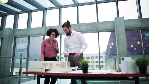 Young architects discussing house model in modern office space