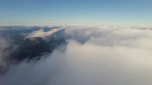 Aerial View From Above of White Puffy Clouds Covering Snowy Mountain Tops in Bright Sunny Day