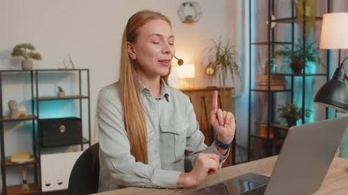Mature Female Customer Service Representative with Headset Using Laptop Computer at Home Office Desk
