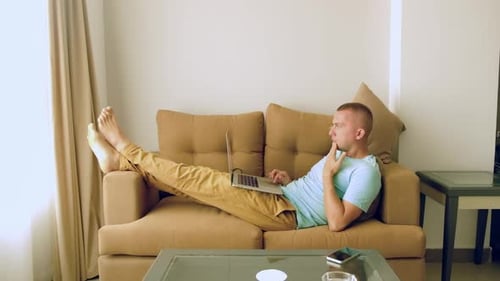 Man Works on Laptop Lying on Sofa