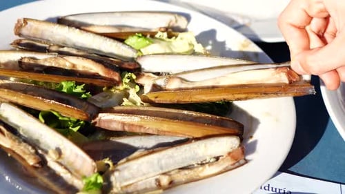 femelle prenant à la main des palourdes grillées sur une assiette blanche avec de la laitue