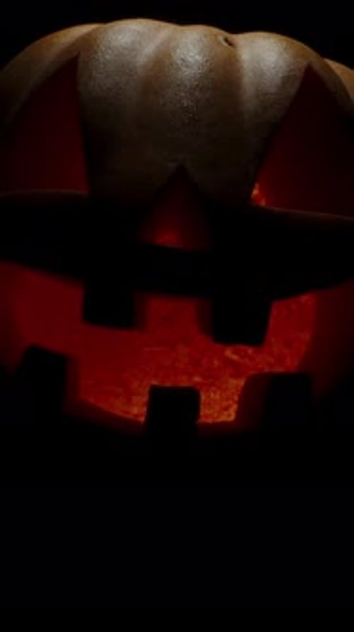 Vertical video. Jack-O'-Lantern Appears from the Darkness. A Halloween Pumpkin Smile and Scary Eyes