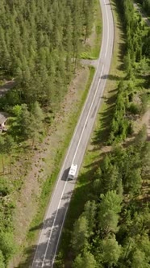 Vertical drone shot tracking a RV motorhome driving in middle of woodlands