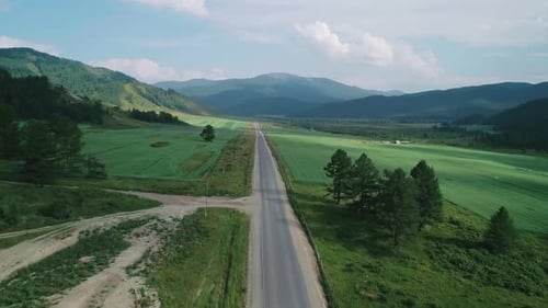 Aerial View of an Asphalt Road in Rural Area Between Green Fields and Hills