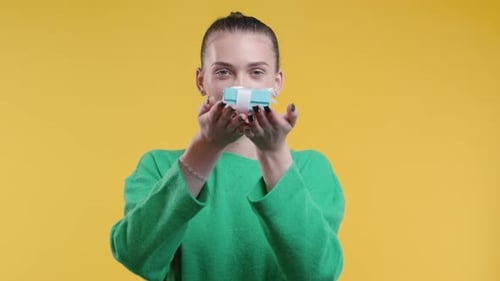 Smiling Woman Holding Birthday Gift on Yellow Background