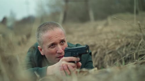 Determined Man Lying on Ground Aiming Handgun in Suspenseful Scene