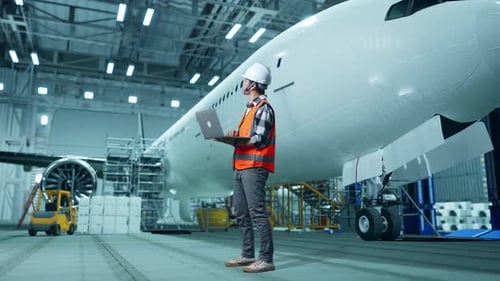 Asian Male Engineer Looking At A Laptop And Looking Around While Aircraft Maintenance