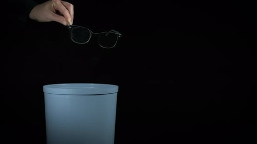 Hand Discards Pair of Glasses into Trash Can