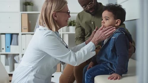 Mature Doctor Examining Thyroid of Cute Little Boy in Medical Office