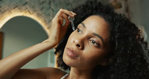 Woman Applying Beauty Serum to Face in Bathroom