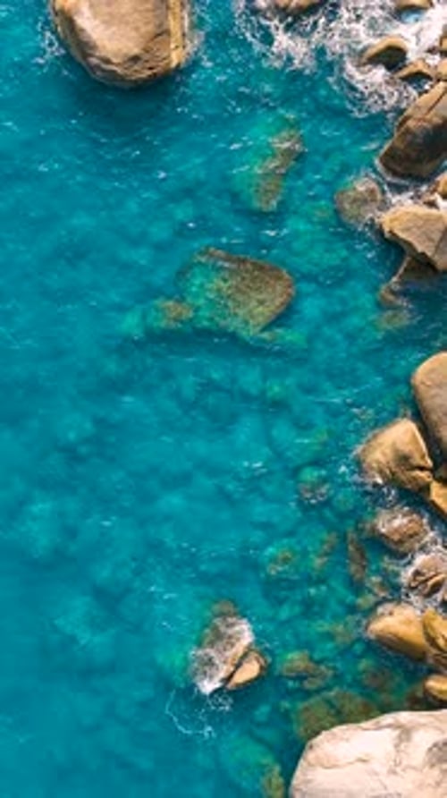 Scenic aerial view of clear blue ocean with rocky coastline. Vertical video