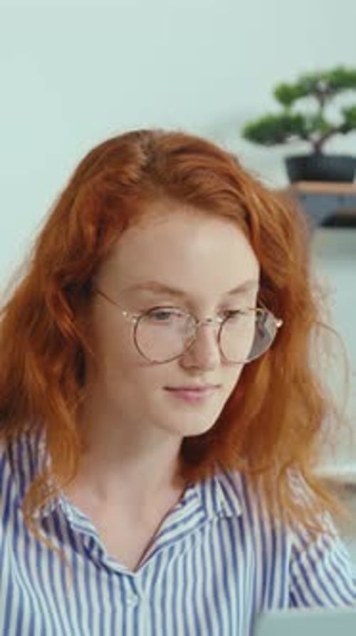 A Redhaired Woman Works Intently on Her Laptop Exuding Focus