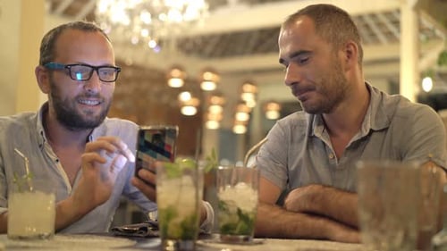 Happy Two Male Friends Talking and Using Smartphone Sitting in Cafe Adult