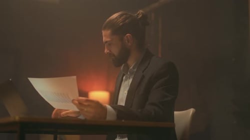 Focused Man Reviews Documents in Dark Office