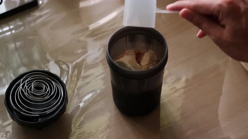 Close-Up Shot: Protein Powder Being Poured Into Shaker Bottle on Kitchen Table Surface
