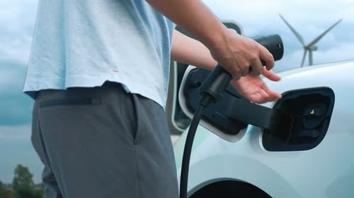 Progressive man charge his EV car by clean energy generate by wind turbine.