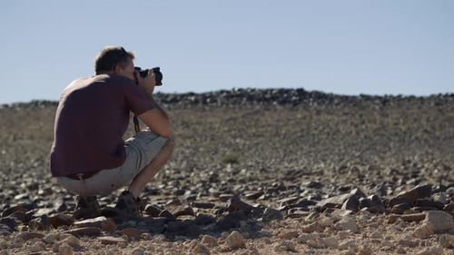 Static hand held shot of a photographer tourist crouched over taking a landscape photo of a desert r
