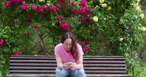 Middle Aged Woman Chatting in Phone in Summer Park on Street Sitting on Bench