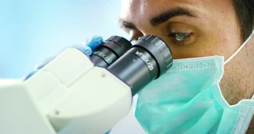 jeune médecin scientifique de sexe masculin propre regardant à travers le microscope pour agrandir les cellules de batteries virales