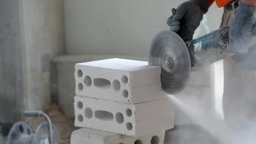 A construction worker cuts a brick using an angle grinder