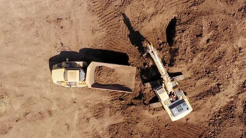 Excavator Filling Truck with Dirt on Construction Site