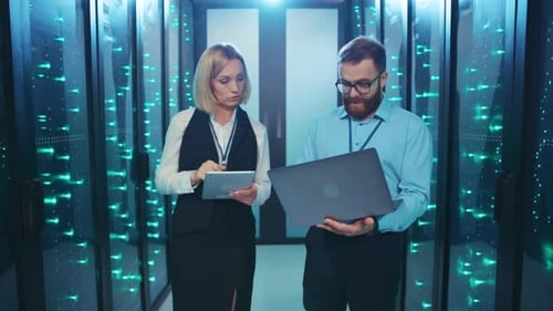 A Man and Woman Stand in a Server Room Observing a Laptop