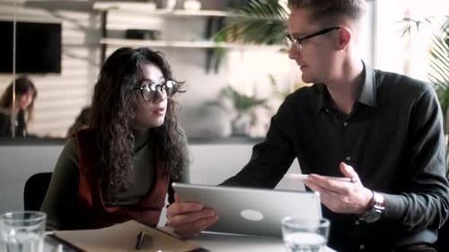 Businessman And Woman Clients Talking Strategy With Tablet At Office Desk In Creative Office