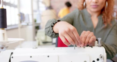Biracial female fashion designer threading sewing machine in studio, slow motion