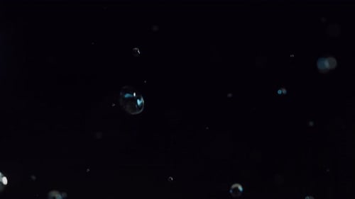 Anmutiger Abstieg von klaren Wassertröpfchen und weißen Bokeh-Partikeln