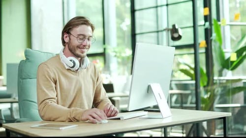 Heureux jeune homme d'affaires employé avec un casque sur le cou travaillant sur un ordinateur dans un lieu de travail moderne