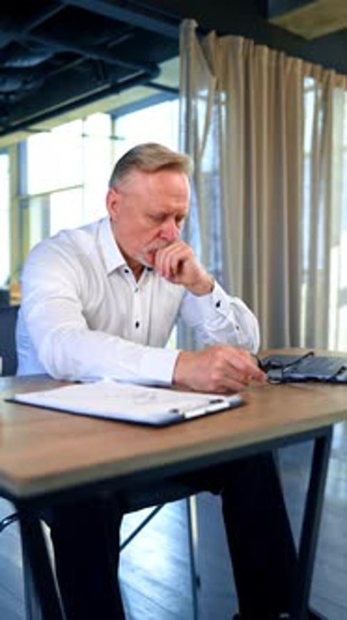 Pensive man sitting at desk in office. Tired exhausted overworking businessman holding his head.
