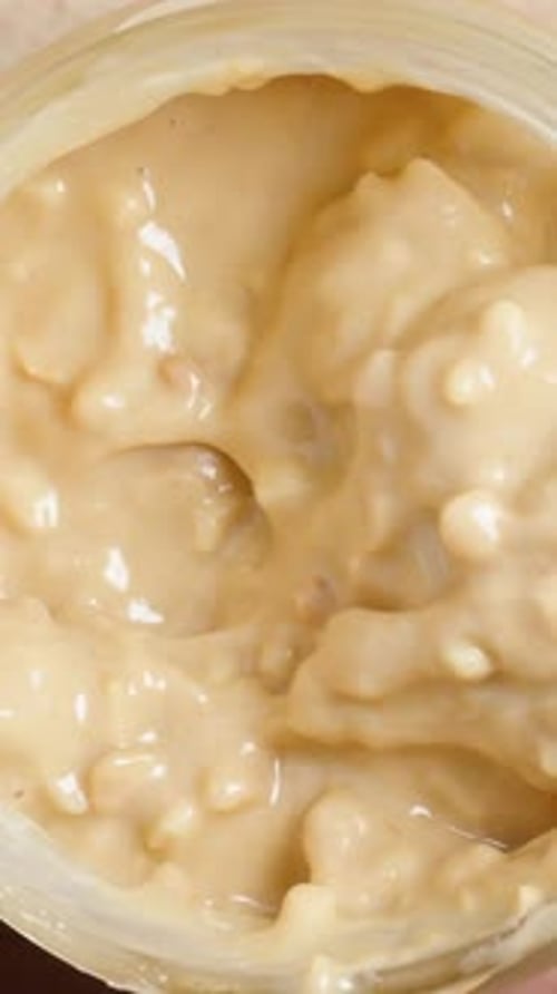 Vertical video. Stirring peanut butter in a jar with a spoon, top view on a wooden table. Close-up.
