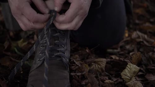 Hiker tying boot laces in autumn leaves close up shot