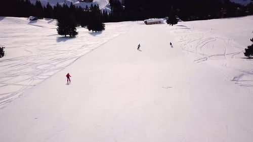 Skiers skiing downhill the ski slope during winter day in the high mountains, aerial view