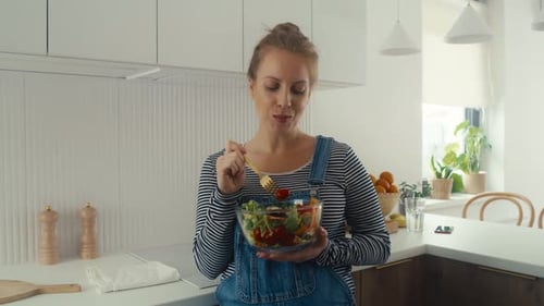 Woman Eats a Salad in Bright Kitchen