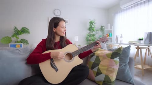 Woman Plays Guitar on Couch in Bright Living Room