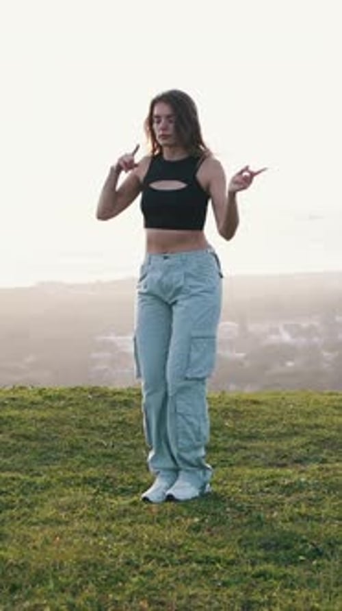 Woman Dances on Grassy Hilltop Overlooking City