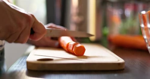 Adult Cuts Carrot on Cutting Board in Kitchen