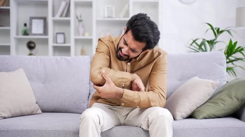 Adult Man Rubbing Sore Elbow Inside Bright Home