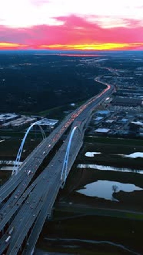 Multiple cars with headlights on move by the Dallas Margaret Mcdermott Bridge at twilight time.