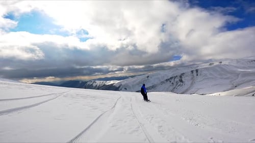 Following a snowboarder in black and blue outfit riding down the slope.