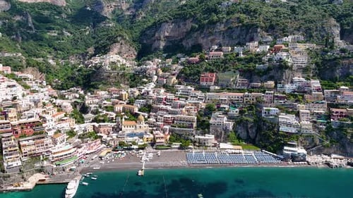 Vue aérienne rotative sur la plage de Positano, entourée de hauts sommets et d'eaux turquoises, Ama