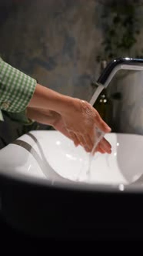 An Upclose Scene Presents a Woman's Hands Positioned Beneath a Water Tap in a Basin