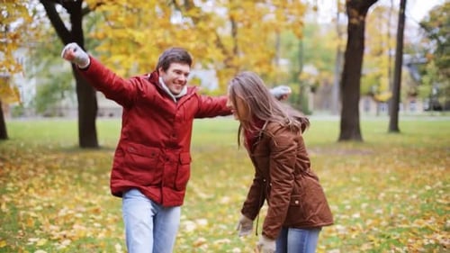 Happy young couple embracing throwing autumn leaves up in central park