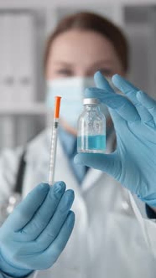 Medical Professional Holds Syringe and Vial of Liquid