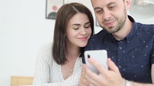 Young Couple Using Mobile Phone Together Indoors