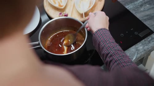 Rear View of Person Stirring Soup in Pot While Adjusting Cooking Temperature
