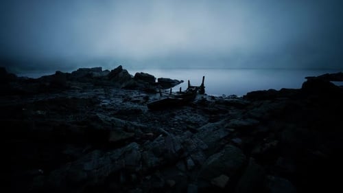 Mysterious Fog Envelops a Lonely Boat on a Rocky Shore at Twilight