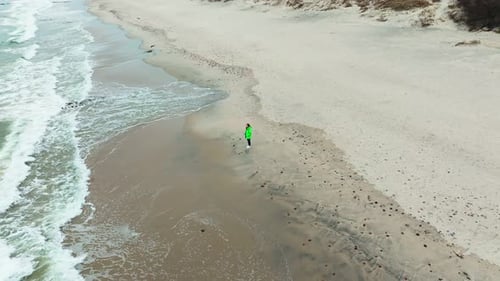 A Woman Walks Along a Tranquil Beach During Winter Surrounded By Soft Sand and Gentle Ocean Waves